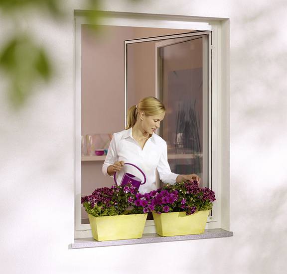 Frau gießt dank komfortabel nutzbarem Insektenschutz-Drehrahmen ihre Blumen auf der Fensterbank von innen aus