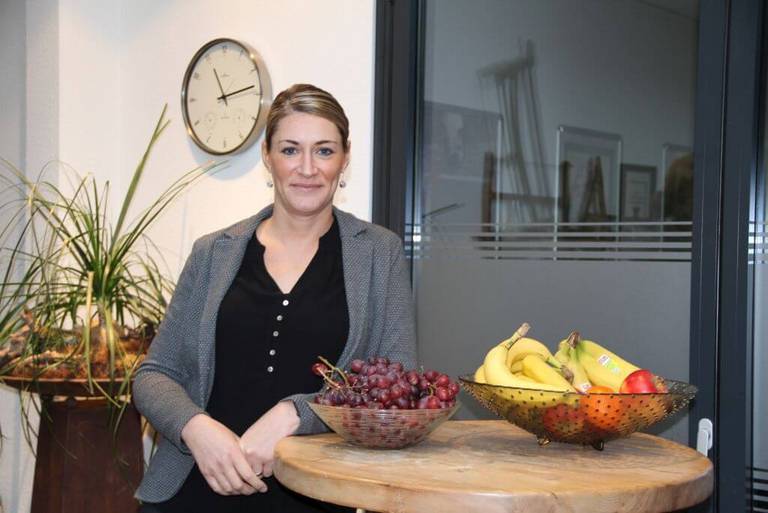 Sarah Schmitz von der Schulz-Dobrick GmbH an Tisch mit Obstkorb angelehnt