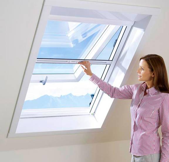 Frau bedient mühelos ihr Insektenschutz für Dachfenster als Rollo am schrägen Dachfenster