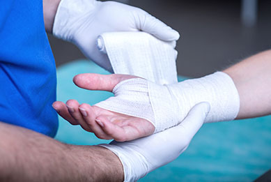 Nahaufnahme einer verletzten Hand, welche von einem Arzt verbunden wird