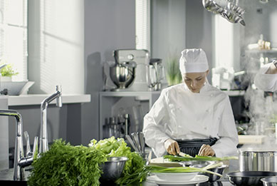Köchin in heller moderner Gastronomie-Großküche bereitet Speisen zu
