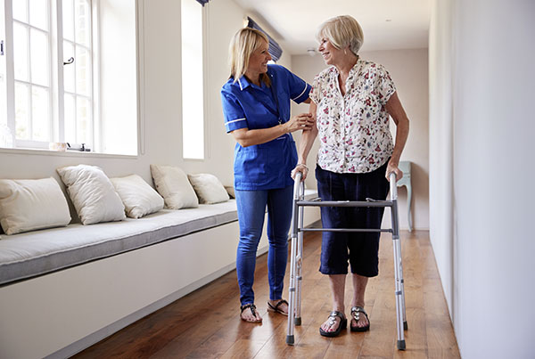 Pflegerin hilft älterer Dame in einem Pflegeheim durch den Flur