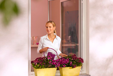 Frau gießt Blumen auf der Fensterbank, da sie mühelos den Drehrahmen öffnen konnte