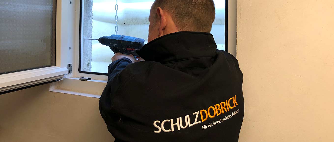 Ein Schulz-Dobrick-Techniker bohrt ein Loch, um die Edelstahlkette für die Lichtschachtsicherung zu montieren.