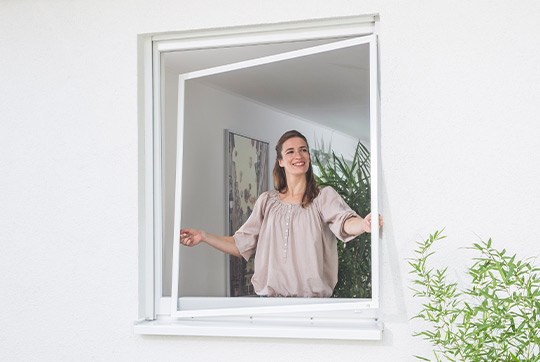 Eine junge Frau entfernt den Insektenschutzspannrahmen aus ihrem Fenster